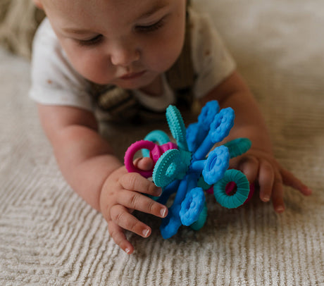 Baby playing with Okee Toy a colorful toy on a textured surface