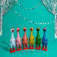 Giant Sparkle Rubber Chicken with red feet on a teal background with decorative string lights.