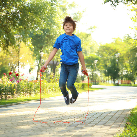 Child jumping rope in a park with trees and flowers in the background