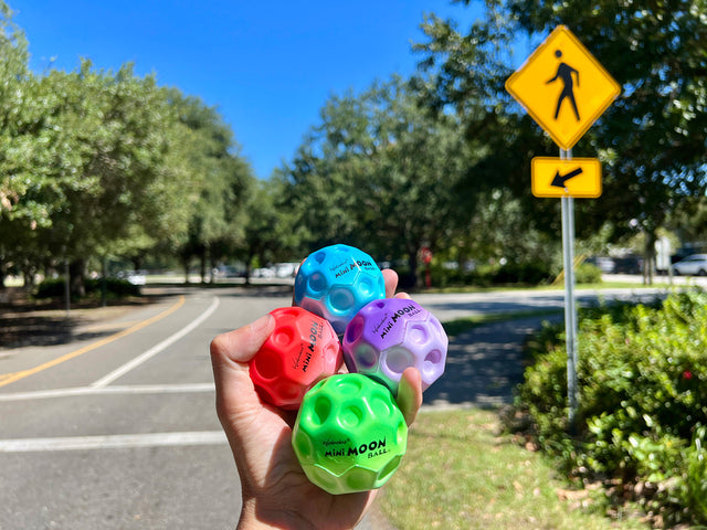 Waboba Mini Moon Balls held by a hand with a road and trees in the background