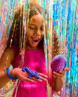 Child holding purple Twiddle Sensory Dragon! in front of colorful tinsel