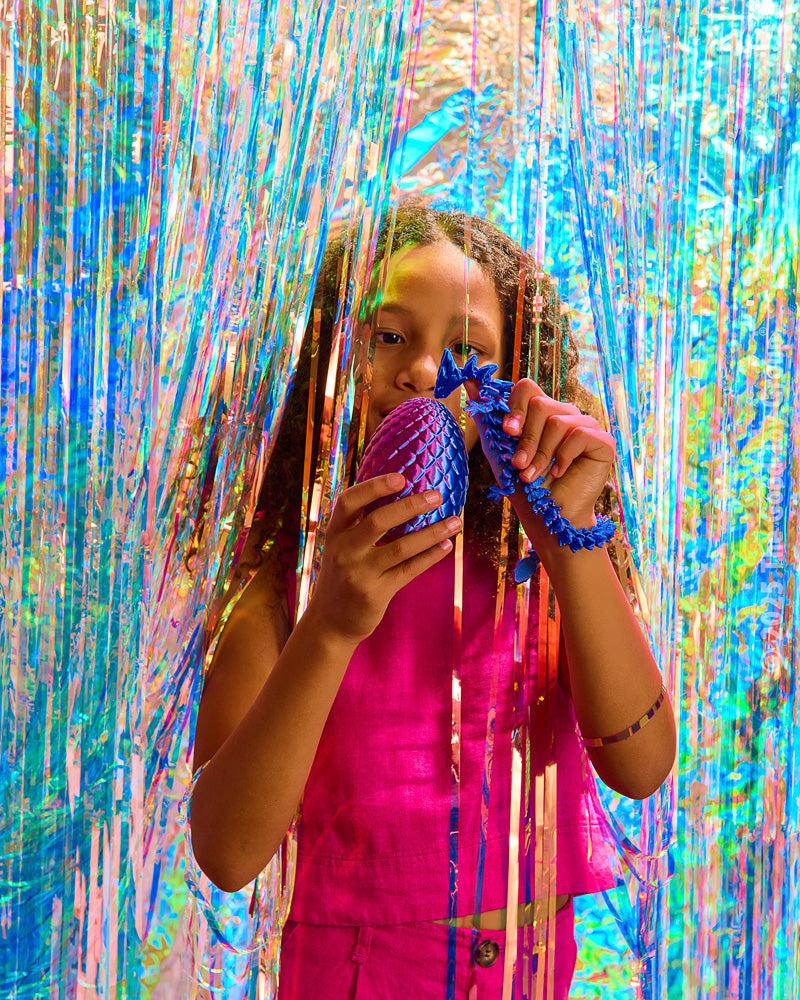 Child holding a blue Twiddle Sensory Dragon in front of a colorful tinsel curtain