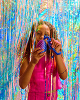 Child holding a blue Twiddle Sensory Dragon in front of a colorful tinsel curtain