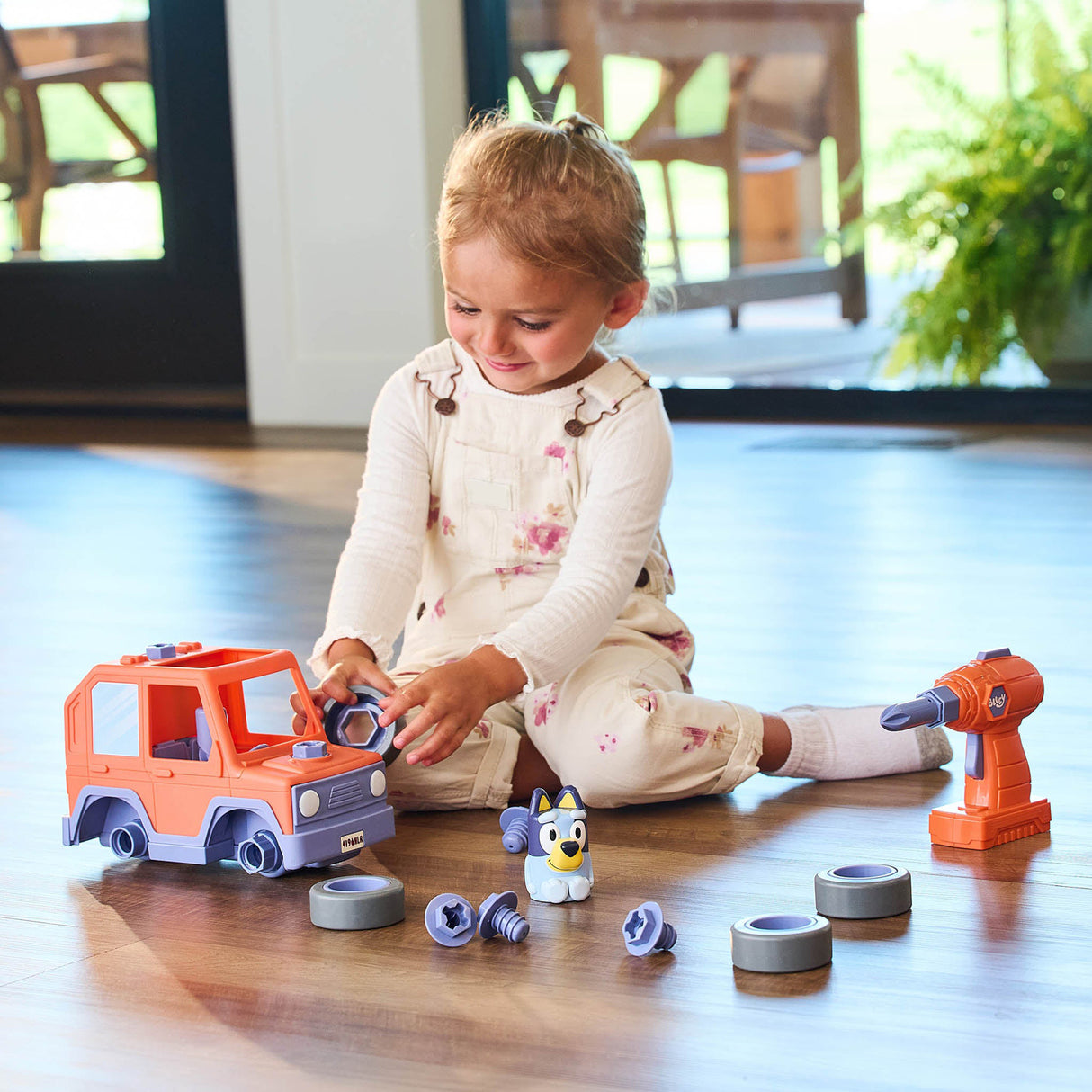 Child playing with toy Bluey Build-A-Buddy Motorized Car and Drill set on a wooden floor