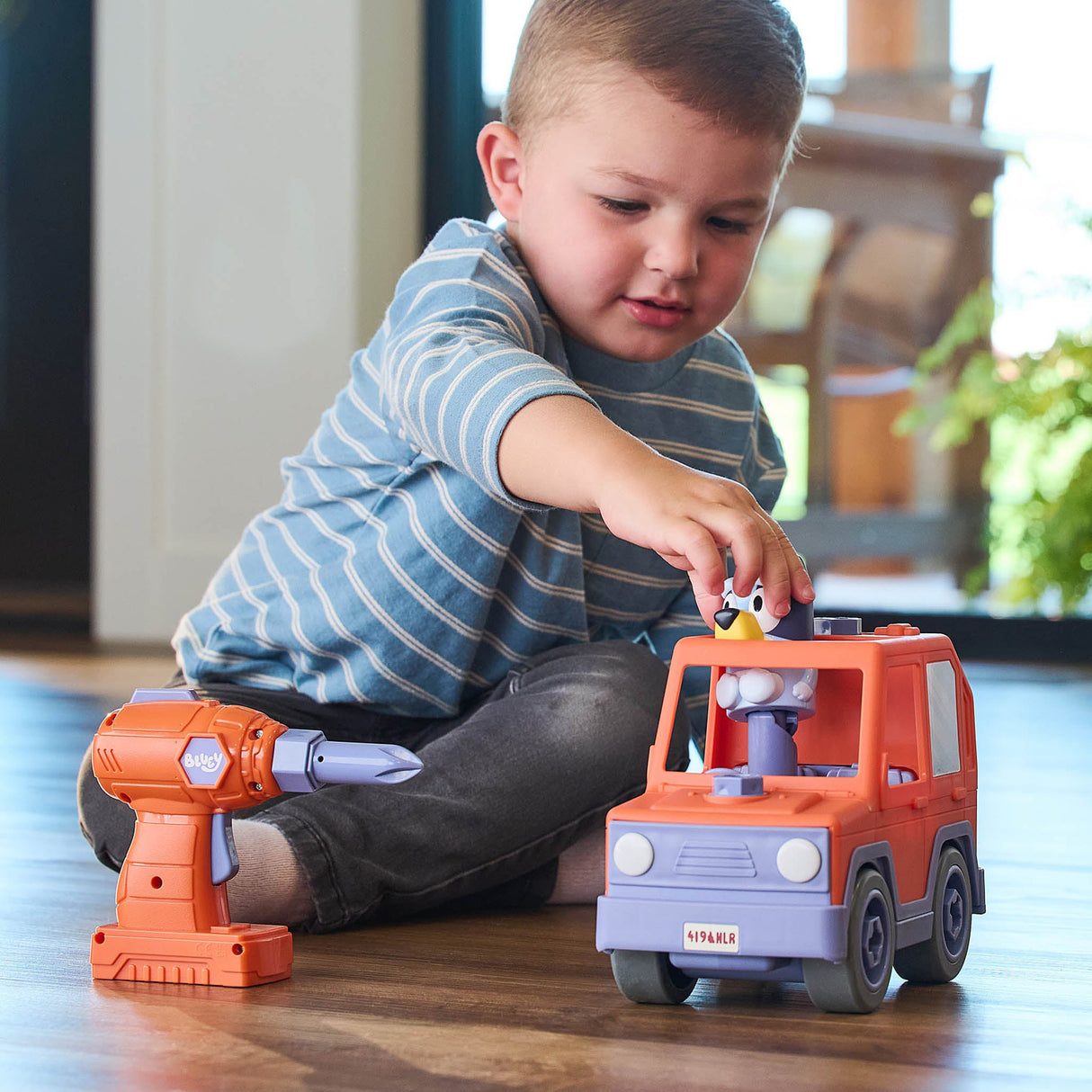 Child playing with toy Bluey Build-A-Buddy Motorized Car and Drill on a wooden floor