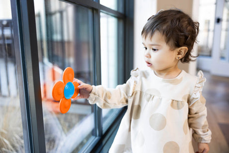 Child playing with a colorful Whirly Squigz Fun Little Spinner! Single near a glass door