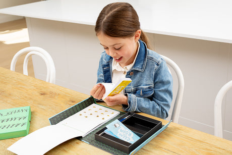 Girl sitting at a table with a Flip Book Kit - Animation In Action, looking at a yellow flip book.