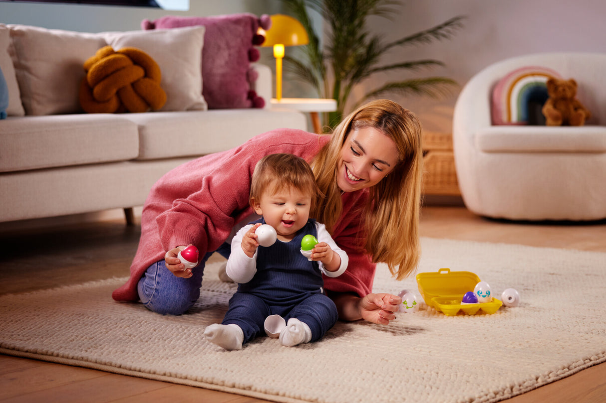 Woman and child playing with Toomies Hide and Squeak Eggs on a rug in a living room