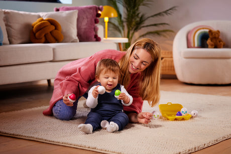 Woman and child playing with Toomies Hide and Squeak Eggs on a rug in a living room