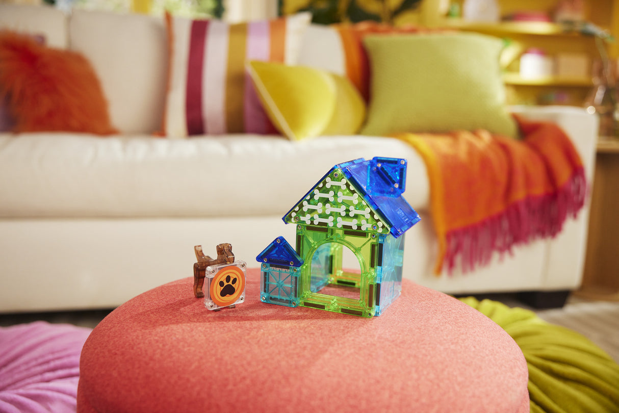 Colorful toy house and dog figurine on a pink ottoman with a patterned sofa in the background